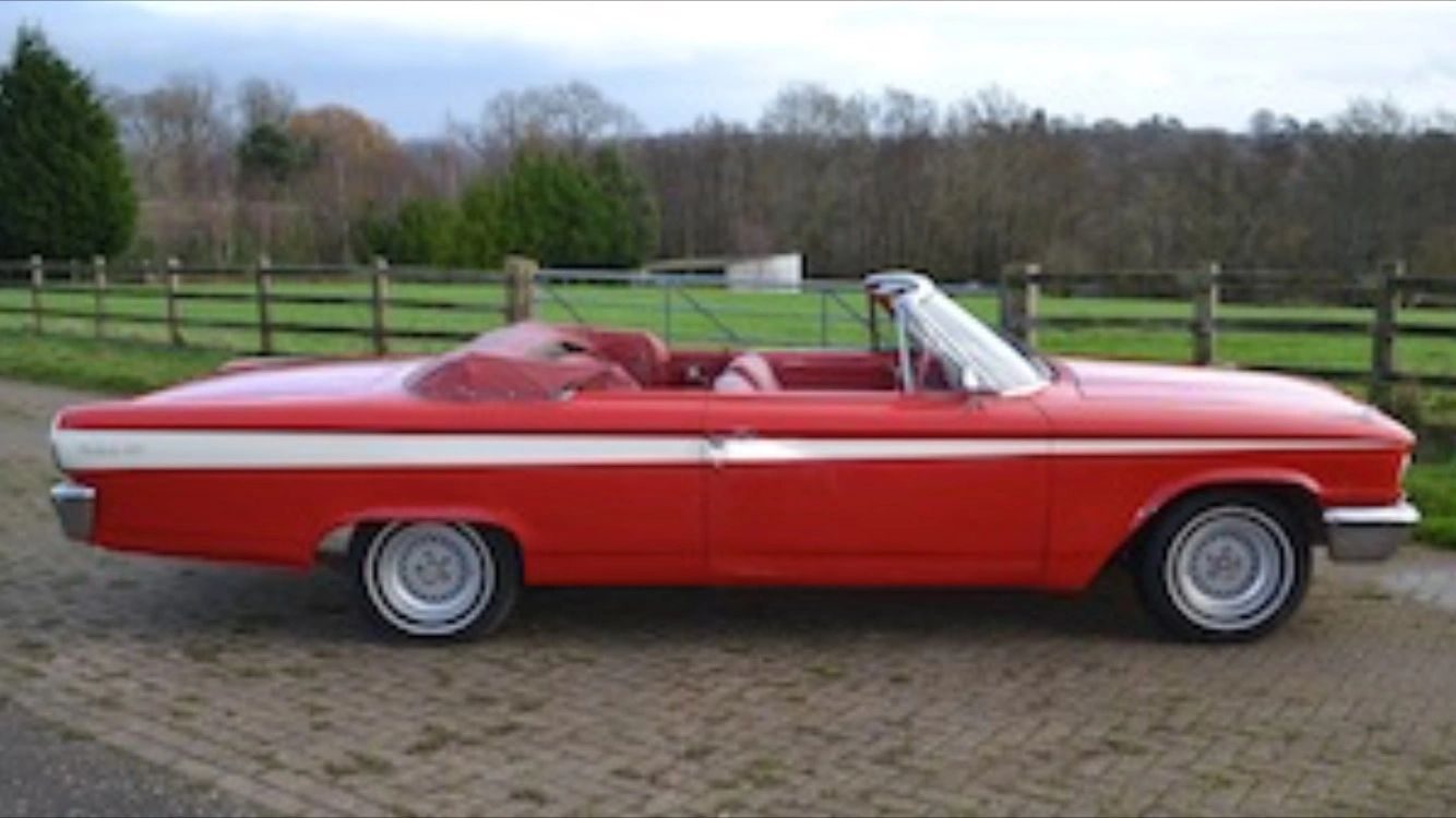 Side view of the red and cream Galaxie convertible with the roof down, on a brick-paved drive