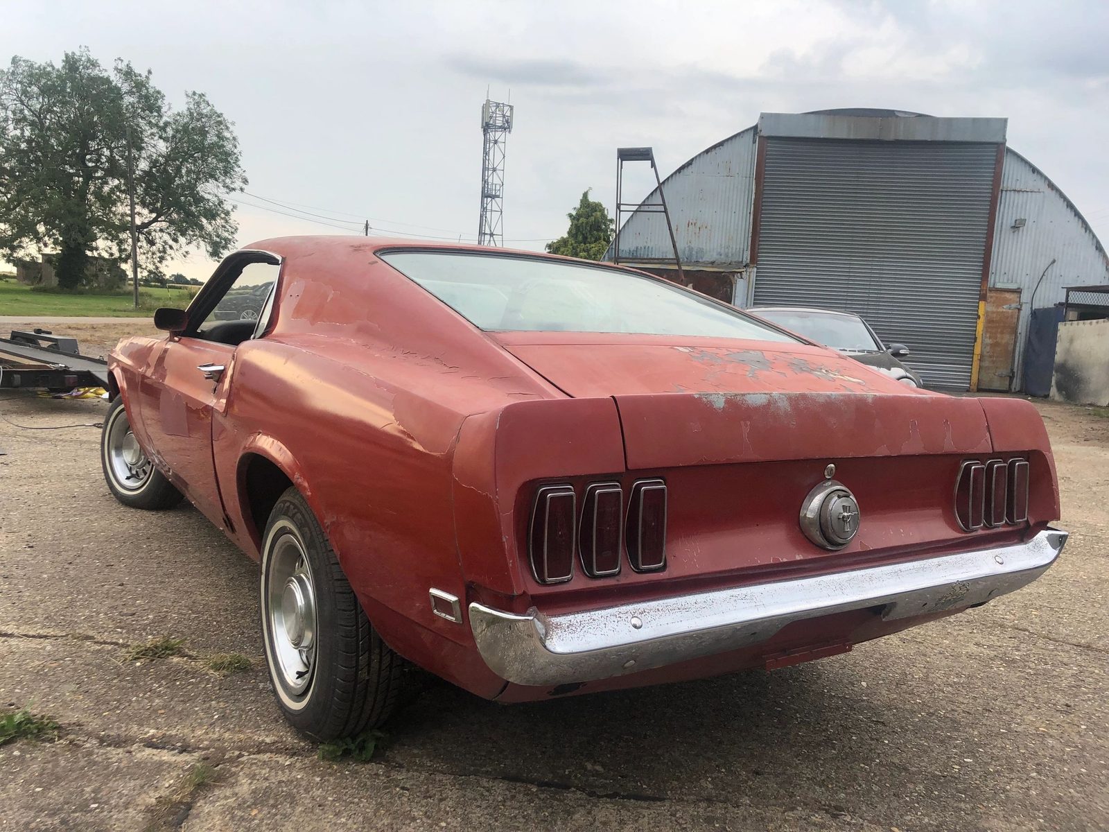 Rear three-quarter view of the red Mach 1 outdoors,, showing the tail lights and chrome bumper