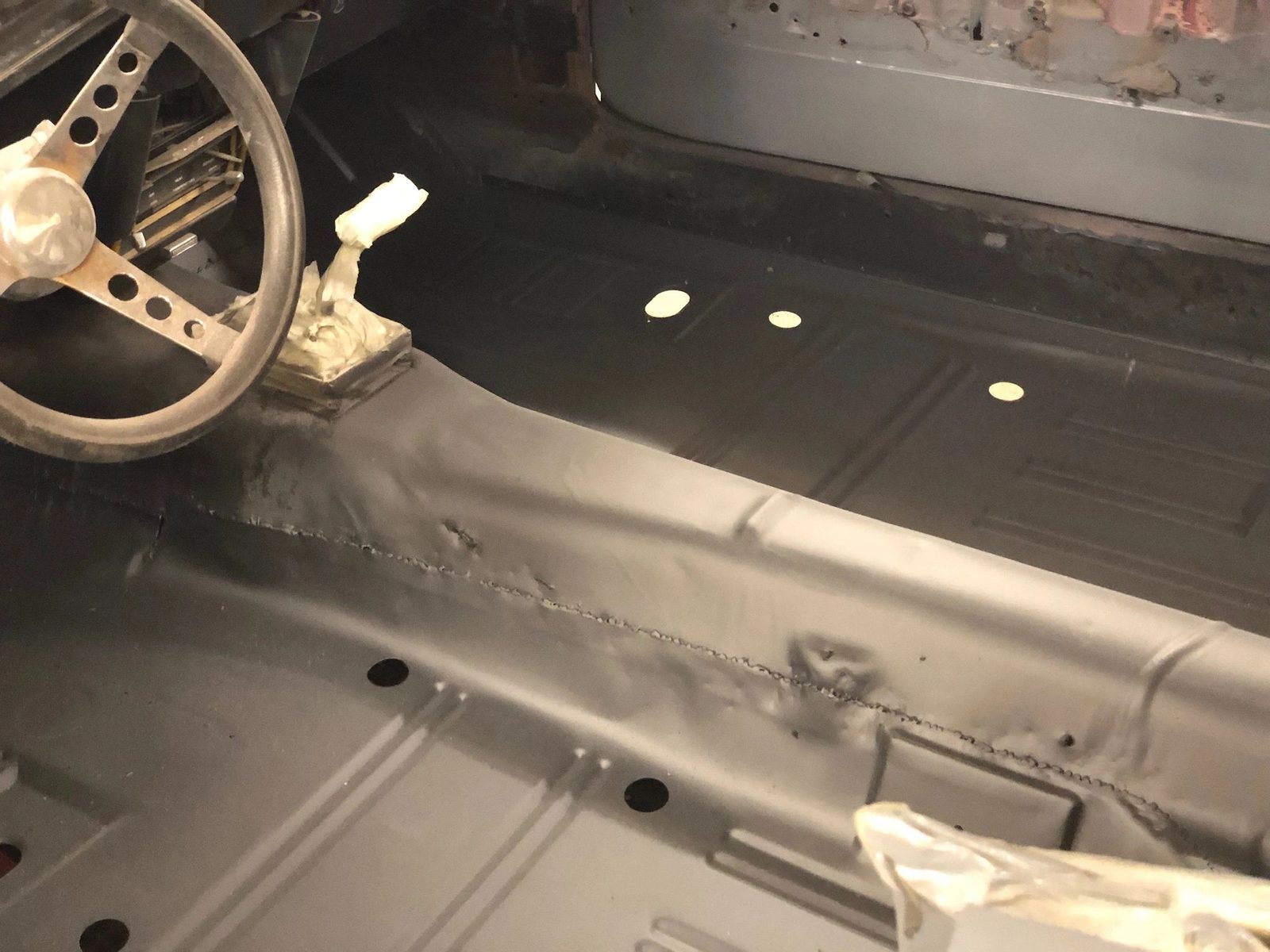 Bare floorpan, transmission tunnel and steering wheel inside the stripped Mustang