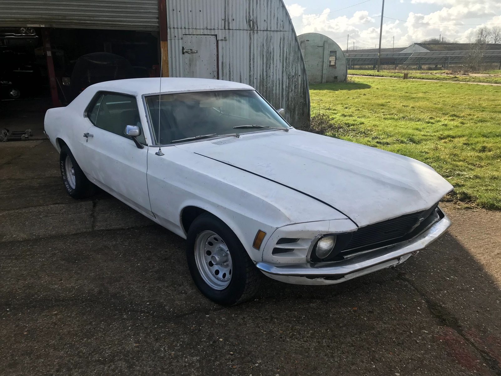 White 1970 Mustang coupe parked outside a workshop barn, seen from the front left